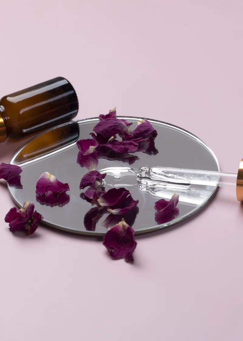 Two serum dropper bottles on a mirror with dried rose petals
